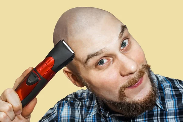 一个秃头的男人，留着胡子，手里拿着剪子，早上在家里用彩色的背景刮胡子 — 图库照片
