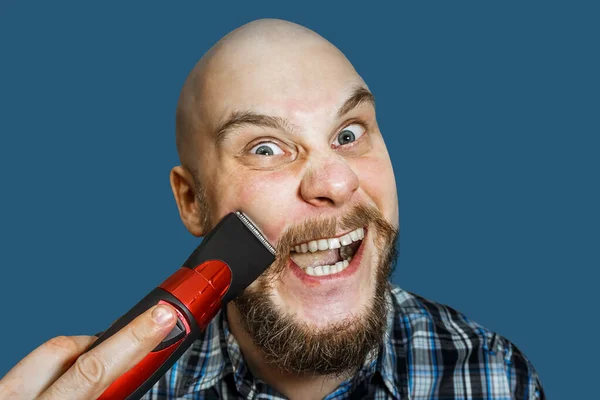 Kopasz fickó szakállal és ollóval a kezében, reggel borotválkozik otthon, színes háttérrel. — Stock Fotó