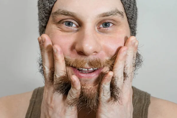 Retrato de un joven barbudo con sombrero se peina la barba con un fondo aislado — Foto de Stock