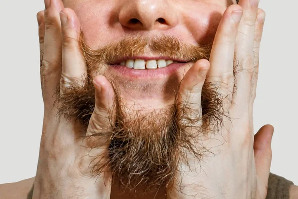 Portret van een jonge man met een baard in een hoed kamt zijn baard handen een geïsoleerde achtergrond — Stockfoto