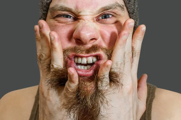 Portrait of a surprised bearded guy in a hat with open mouth, comb his beard with his hands and fingers in the studio — Stock Photo, Image