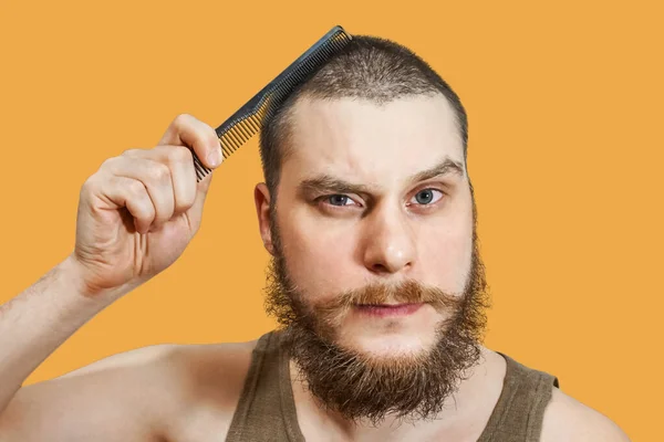 Cara barbudo penteando sua cabeça careca com uma escova de cabelo no estúdio em um fundo isolado branco — Fotografia de Stock