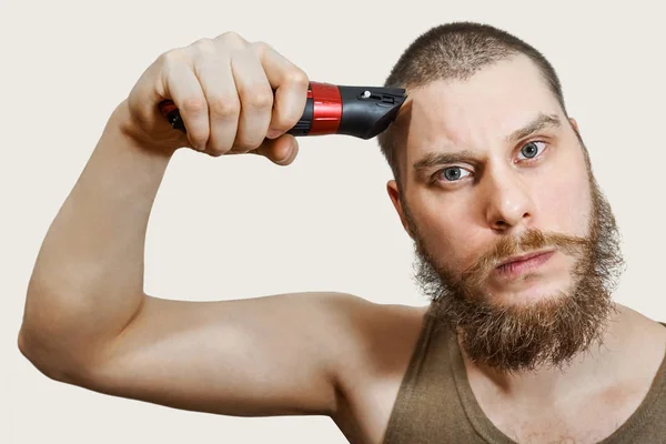 Ritratto di un barbuto che si taglia la barba, capelli sulla testa e baffi con un clipper su uno sfondo isolato — Foto Stock