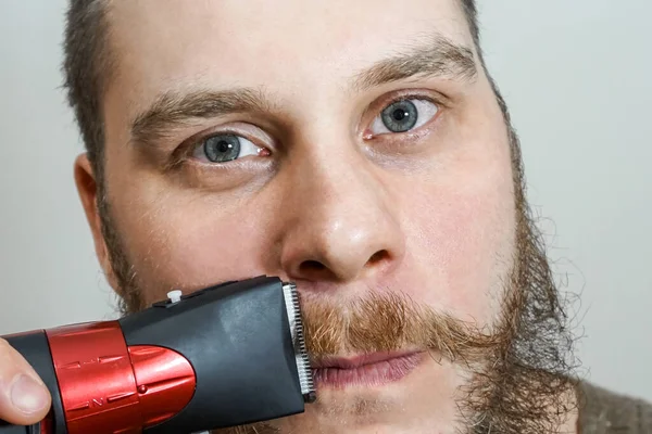 Портрет бородатого хлопця розрізає бороду, волосся на голові і вуса за допомогою затискача на ізольованому фоні — стокове фото