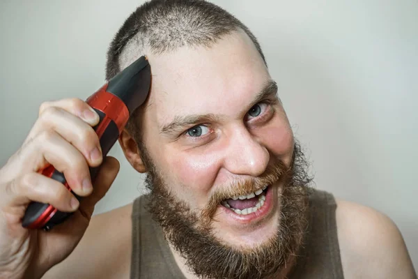 Porträt eines bärtigen Mannes schneidet sich Bart, Haare auf dem Kopf und Schnurrbart mit einem Clipper auf isoliertem Hintergrund — Stockfoto