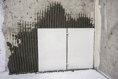 İşçi el, çentikli malayla duvara fayanslar yapıştırıyor..