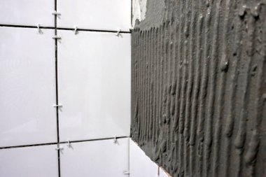 İşçi el, çentikli malayla duvara fayanslar yapıştırıyor..