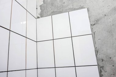 İşçi el, çentikli malayla duvara fayanslar yapıştırıyor..