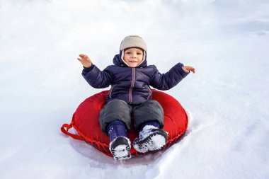 Mutlu, neşeli, güzel çocuk kışın kırmızı bir boruyla dağdan iniyor.