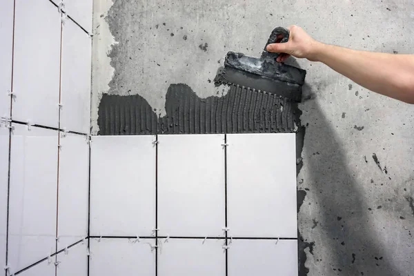 La main ouvrière met des carreaux adhésifs sur le mur avec la truelle entaillée . — Photo