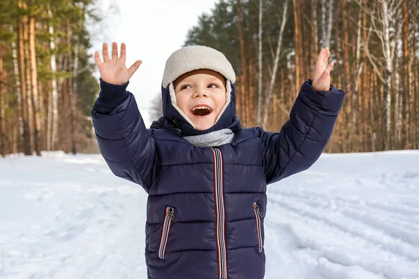 Ritratto di un bambino felice getta neve, fiocchi di neve nell'aria in inverno freddo sullo sfondo di cumuli di neve — Foto Stock