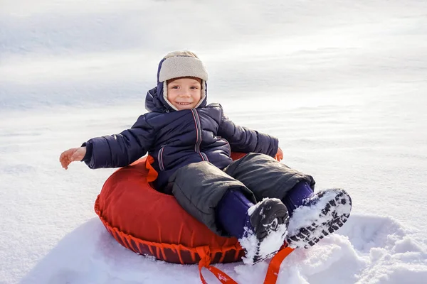 Fröhlich fröhlich schöne Kind reitet vom Berg auf einem roten Schlauch im Winter — Stockfoto