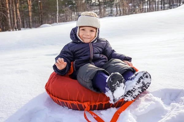 Happy joyful beautiful child boy rides from the mountain on a red tubing in winter — Stock Photo, Image