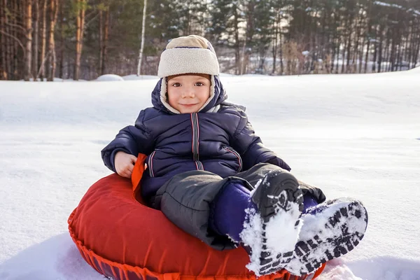 Mutlu, neşeli, güzel çocuk kışın kırmızı bir boruyla dağdan iniyor. — Stok fotoğraf