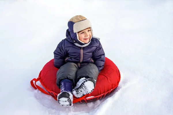Fröhlich fröhlich schöne Kind reitet vom Berg auf einem roten Schlauch im Winter — Stockfoto