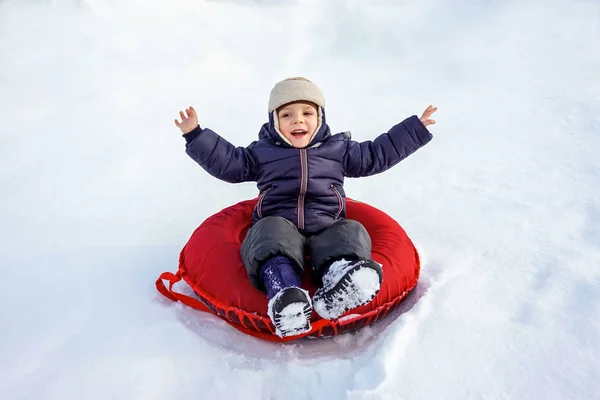 Glad glad glad vacker pojke rider från berget på en röd slang på vintern — Stockfoto