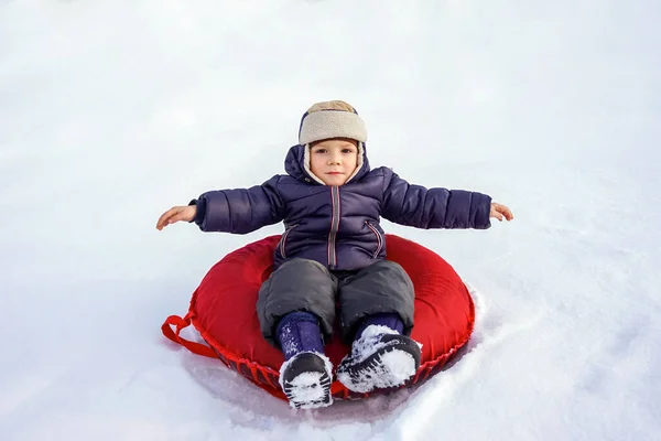 Fröhlich fröhlich schöne Kind reitet vom Berg auf einem roten Schlauch im Winter — Stockfoto