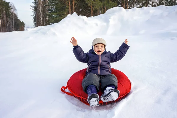 Fröhlich fröhlich schöne Kind reitet vom Berg auf einem roten Schlauch im Winter — Stockfoto