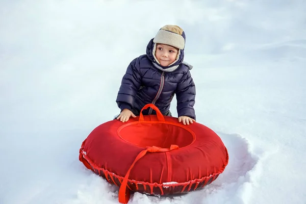 Fröhlich fröhlich schöne Kind reitet vom Berg auf einem roten Schlauch im Winter — Stockfoto