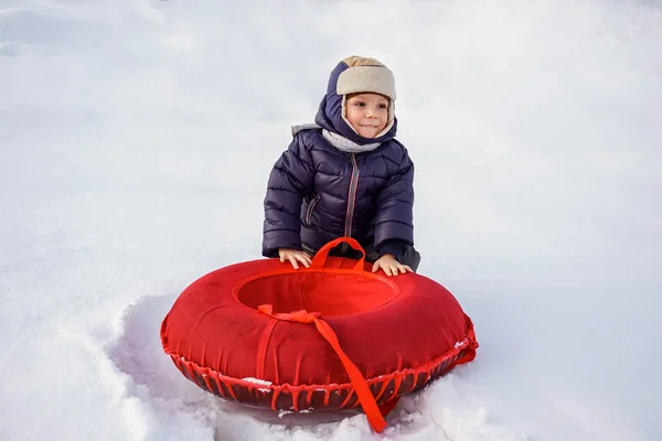 Fröhlich fröhlich schöne Kind reitet vom Berg auf einem roten Schlauch im Winter — Stockfoto