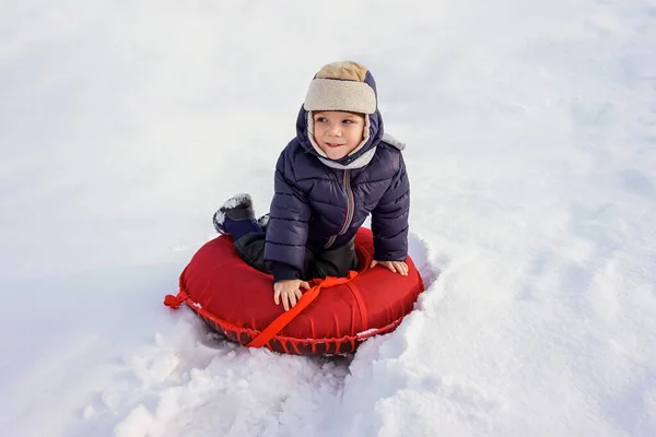 Šťastný radostné krásné dítě chlapec vyjíždí z hory na červeném tubing v zimě — Stock fotografie