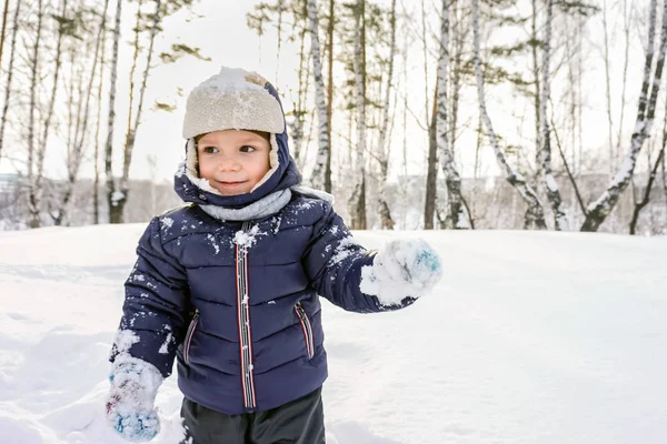 Portrait of a happy child boy throws snow, snowflakes in the air in cold winter against snowdrifts — Stock Photo, Image