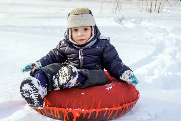 Happy joyful beautiful child boy rides from the mountain on red tubing in winter — Stock Photo, Image