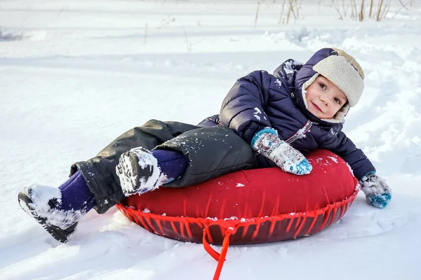 Heureux joyeux beau enfant garçon promenades de la montagne sur tube rouge en hiver — Photo