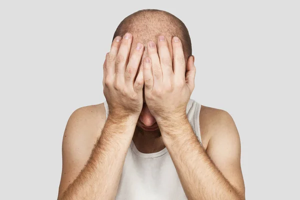 Ένας φαλακρός άντρας καλύπτει το πρόσωπό του με τα χέρια του και κλαίει από απελπισία, μοναξιά και προβλήματα σε γκρι φόντο. — Φωτογραφία Αρχείου