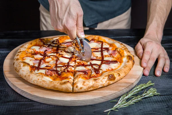 Cortar pizza barbacoa con salami, carne, jamón, salchicha, pimientos, champiñones, tomate, queso con cortador en una tabla de madera — Foto de Stock