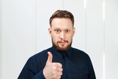 Sakallı adam baş parmağını gösteriyor. Yakışıklı bir yetişkinin portresi.