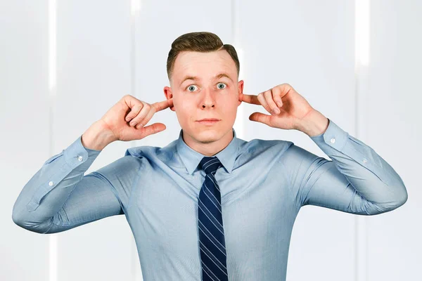 Young guy businessman cover ears from noise. dressed in blue shirt