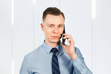 Mavi gömlekli ve kravatlı genç işadamının portresi, cep telefonuyla konuşuyor.