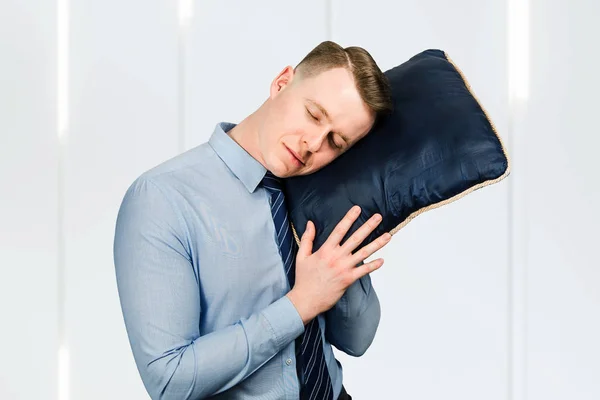 Fiatal srác üzletember kék ingben és nyakkendőben alszik egy párnával a kezében. — Stock Fotó