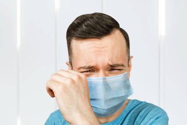 Mutsuz, ağlayan, koruyucu maske takan genç adam virüs enfeksiyonunu ve kirliliği önler..