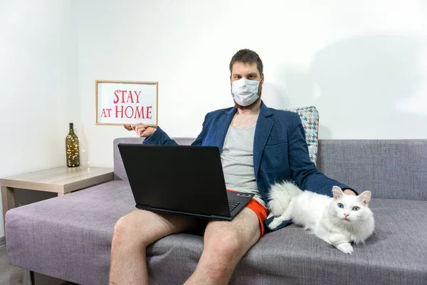 man wear protective medical mask study online with video call. guy watch laptop at home with cat. Covid-19 coronavirus