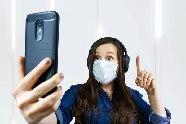 woman in medical mask doing phone video call from home during self isolation and quarantine at corona virus, covid-19.
