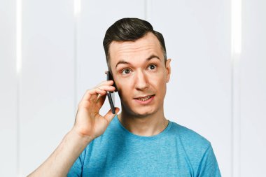 Mavi tişörtlü genç beyaz adam telefonda konuşuyor..