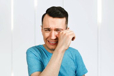 Ağlayan genç adam elleri açık, ağzı açık, mavi tişört giymiş..