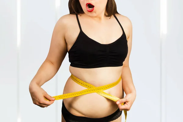 Young fat woman in underwear with measuring tape and fat folds.