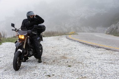 Sürücü, motorsikletle dağlarda maceralı bir yolculuğa çıkmak için sisin ötesini görmeye çalışıyor. Macera gezisi projesi.
