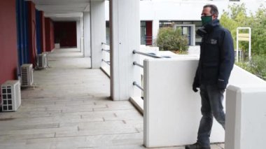 Koruyucu maskesi ve eldivenleri takan adam kapalı bir binaya geliyor. Maske ve eldiven takıyor.