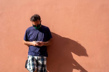 Elinde cep telefonu tutan, cerrahi tıbbi maskeli, olgun, yakışıklı bir adam.,