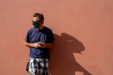 Elinde cep telefonu tutan, cerrahi tıbbi maskeli, olgun, yakışıklı bir adam.,