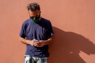 Elinde cep telefonu tutan, cerrahi tıbbi maskeli, olgun, yakışıklı bir adam.,
