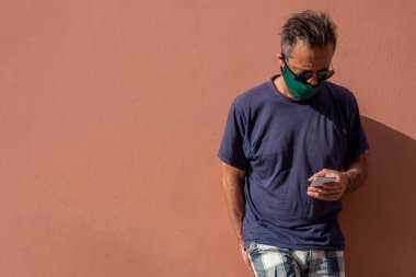 Elinde cep telefonu tutan, cerrahi tıbbi maskeli, olgun, yakışıklı bir adam.,