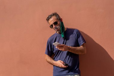 Yakışıklı, olgun bir adam, sıcaktan bıkmış koruyucu maskesini çıkarmış ve sigara içiyor. ..