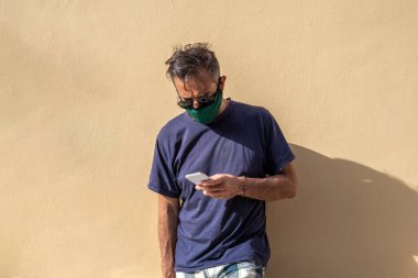 Elinde cep telefonu tutan, cerrahi tıbbi maskeli, olgun, yakışıklı bir adam.,