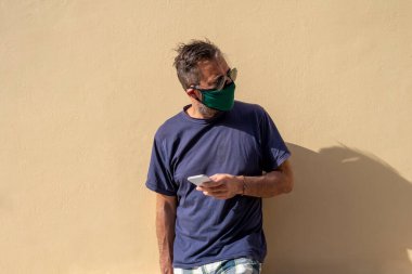 Elinde cep telefonu tutan, cerrahi tıbbi maskeli, olgun, yakışıklı bir adam.,