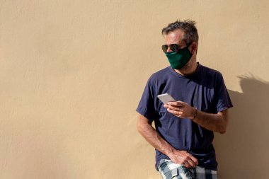Elinde cep telefonu tutan, cerrahi tıbbi maskeli, olgun, yakışıklı bir adam.,